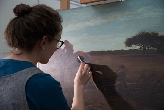 Image shows a paintings conservator using a cotton swab to remove varnish from a landscape with two figures and a horse.